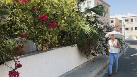 Beautiful woman walks on the street and sniff flowers on bush Stock Footage