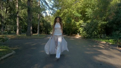 A beautiful woman in a white suit is walking along the path in the park. Stock Footage