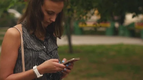 Beautiful woman writes a message walking in summer in the park Stock Footage