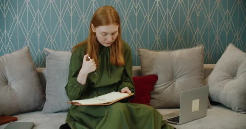 Beautiful woman writes notes in a notebook sitting on the couch at home. Stock Footage 156570907