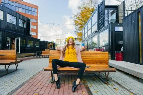Beautiful woman in yellow beret sits on the street on the bench, depicts emot Stock Photos
