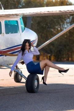 Beautiful young Asian girl sitting on the wheel of an airplane. Stock Photos