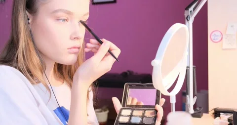Beautiful young blonde girl is doing makeup in front of a mirror in her room Stock Footage 166312002