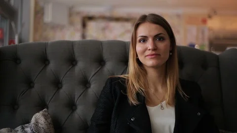 Beautiful young blonde in a jacket on the couch looking at the camera Vidéo 111580050