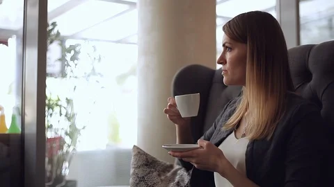Beautiful young blonde thoughtfully drinking coffee and looking out the window Stock Footage 111591003