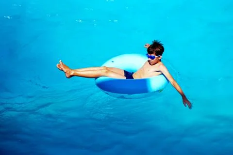 Beautiful young boy with inflatable ring relaxing in blue swimming pool Stock Photos