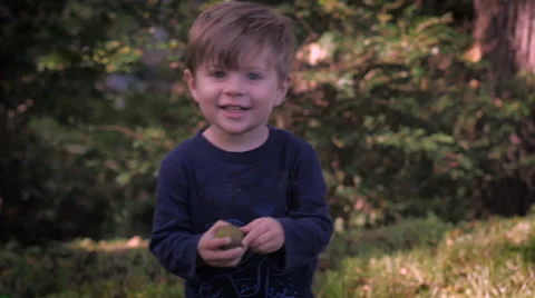 A beautiful young boy picks something up, smiles, and walks toward the camera. Stock Footage 55359657