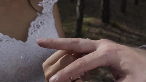 A beautiful young bride gently puts a ring made of gold on her groom's hand on a Stock Footage 306145955