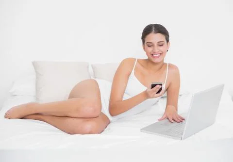 Beautiful young brown haired model in white pajamas using a mobile phone Stock Photos