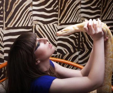 Beautiful young brunette holding a python and kissing him Stock Photos