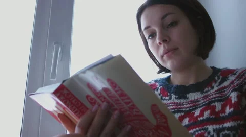 Beautiful young brunette woman reading book wearing knitted sweater sitting home Stock Footage 59019876