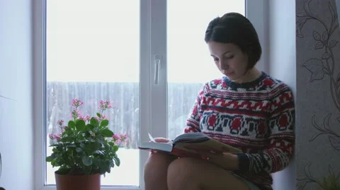 Beautiful young brunette woman reading book wearing knitted sweater sitting home Video stock 59079822