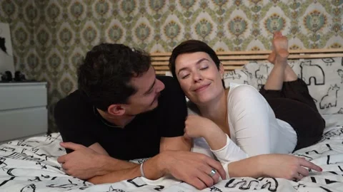 The beautiful young couple is lying on the bed and kissing. Stock Footage 229654280