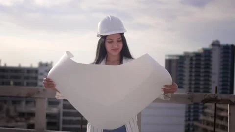 Beautiful young female designer, architect, looks at plan unfolded on paper, dra Stock Footage 240302453