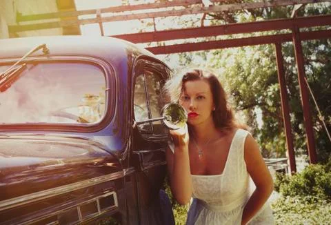 Beautiful young female is fixing her make-up near the vintage car. Stock Photos