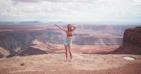 Beautiful young female model dancing and waving peace signs on edge of cliff Stock Footage 167338091