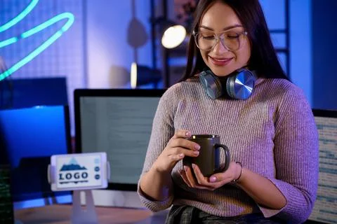 Beautiful young female programmer with cup of coffee near her workspace in mo Stock Photos