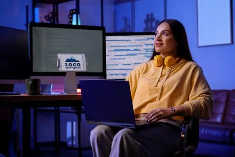 Beautiful young female programmer working with laptop in modern office at nig Stock Photos