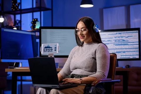 Beautiful young female programmer working with laptop in modern office at nig Stock Photos
