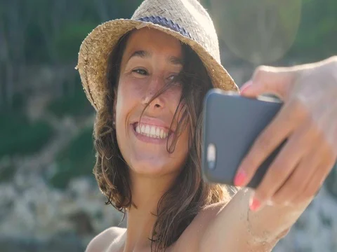 Beautiful young girl doing selfie at the sea, smiling waving at the camera Stock Footage