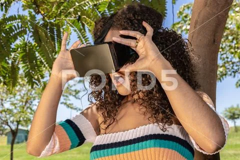 A beautiful young girl plays a game wearing virtual reality glasses on the pa Stock Photos