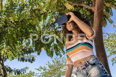 A beautiful young girl plays a game wearing virtual reality glasses on the pa Stock Photos
