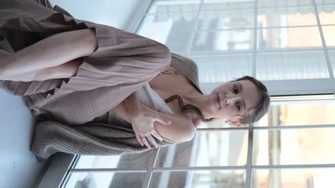 Beautiful young girl posing for the camera while sitting near a large window Video stock 275452359