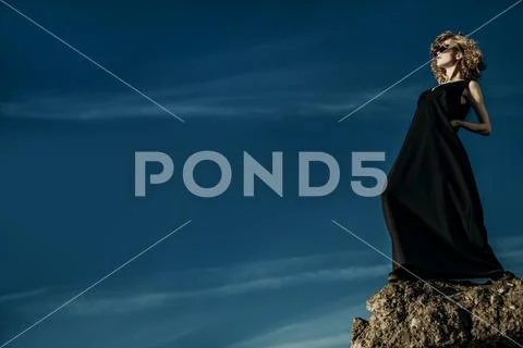 A beautiful young girl is posing outside in a black dress on the top of a roc Stock Photos