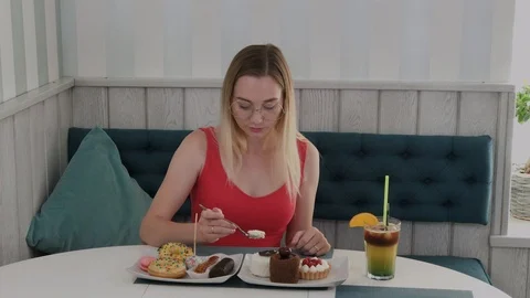 Beautiful young girl sits at a table in a cafe and eats sweet fresh desserts Video stock 116690153