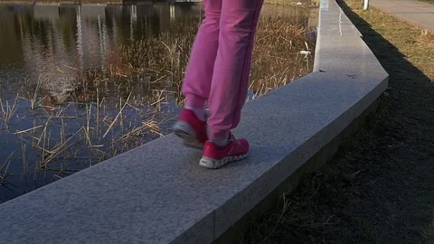 Beautiful young girl walking stone parapet lake shore, evening. Legs, Pink Stock Footage