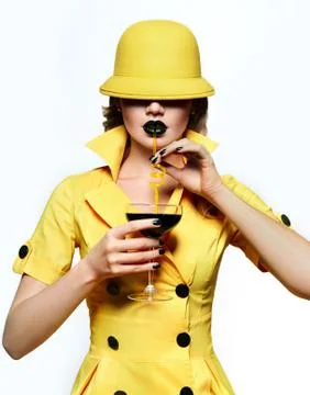 A beautiful young girl in a yellow hat and yellow dress is holding a glass with  Stock Photos