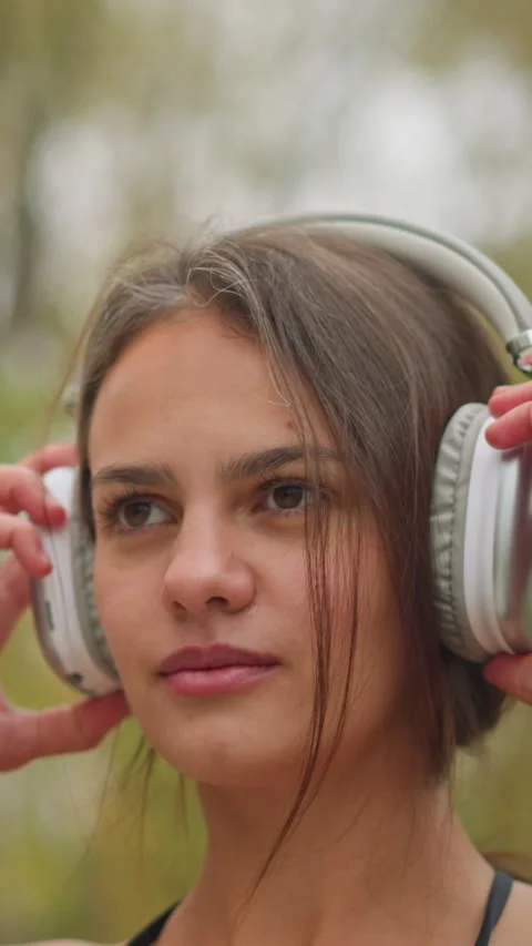 Beautiful young lady focused while adjusting headphones outdoors Video stock 318576742