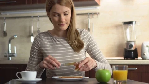 Beautiful young making bread and butter with jam. Breakfast with juice and Stock Footage 71177187