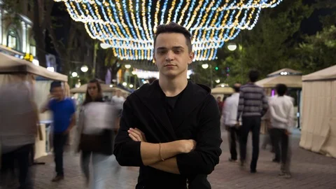 Beautiful young man looking at camera, closeup. Moving crowd of people blurred Stock Footage 95624225