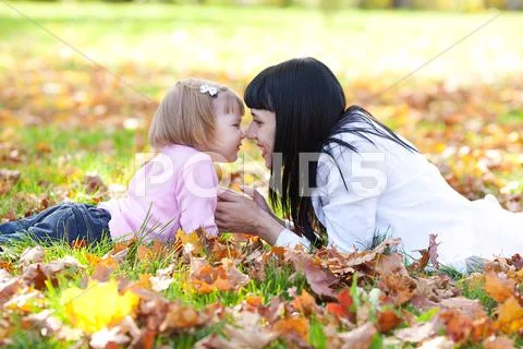 Beautiful young mother and her daughter lying on the autumn leaves Stock Photos