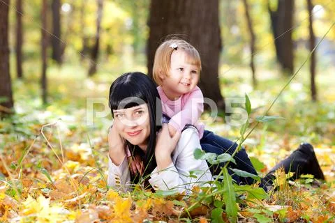 Beautiful young mother and her daughter lying on the autumn leaves Stock Photos