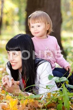 Beautiful young mother and her daughter lying on the autumn leaves Stock Photos