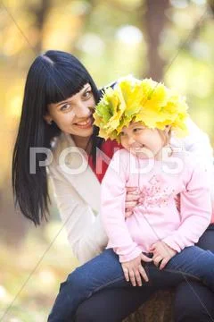 Beautiful young mother holding her daughter in a wreath of maple leaves Stock Photos