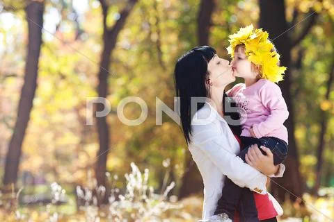 Beautiful young mother holding her daughter in a wreath of maple leaves Stock Photos