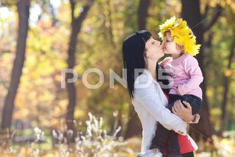 Beautiful young mother holding her daughter in a wreath of maple leaves Stock Photos