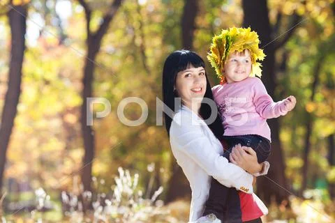 Beautiful young mother holding her daughter in a wreath of maple leaves Stock Photos