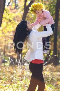 Beautiful young mother holding her daughter in a wreath of maple leaves Stock Photos