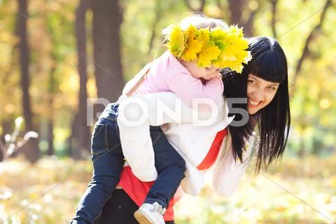 Beautiful young mother holding her daughter in a wreath of maple leaves on ba Stock Photos