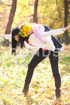 Beautiful young mother holding her daughter in a wreath of maple leaves on ba Stock Photos