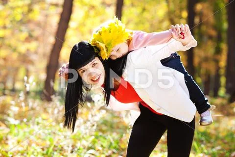 Beautiful young mother holding her daughter in a wreath of maple leaves on ba Stock Photos