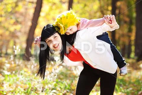 Beautiful young mother holding her daughter in a wreath of maple leaves on ba Stock Photos