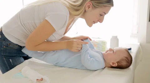 Beautiful young mother undressing her baby son lying on changing table Stock Footage