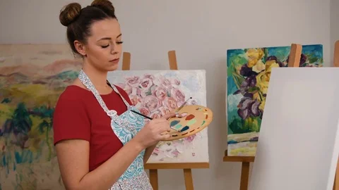 Beautiful young painter holding a brush in her hands and mixing colors on Stock Footage 74195136