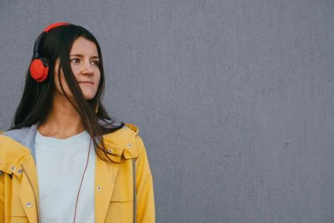 Beautiful young sad lady using headphones and listening music against gray wa Stock Photos