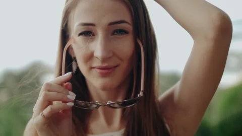 A beautiful young smiling long-haired girl in sunglasses looks at the camera and Stock Footage 130283000